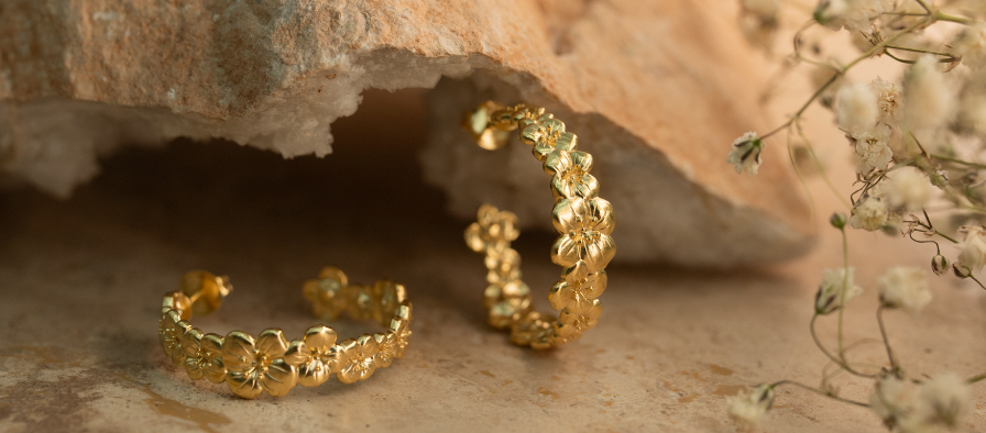 Gold hoop earrings on a stone surface with small white flowers.